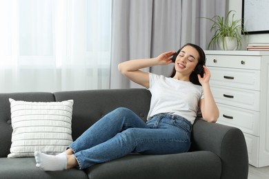 Happy woman in headphones enjoying music on soft sofa at home