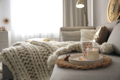 Photo of Cup of drink and burning candles on sofa in room, space for text. Interior elements