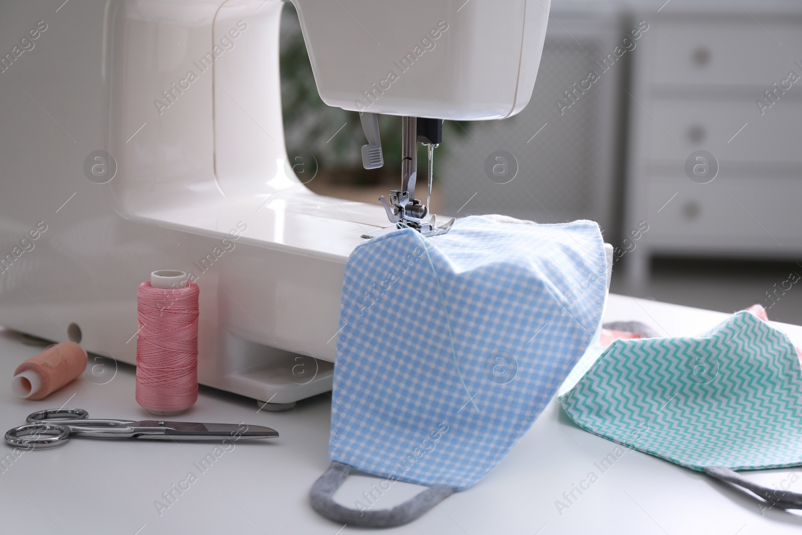Photo of Sewing machine with cloth mask on white table indoors, closeup
