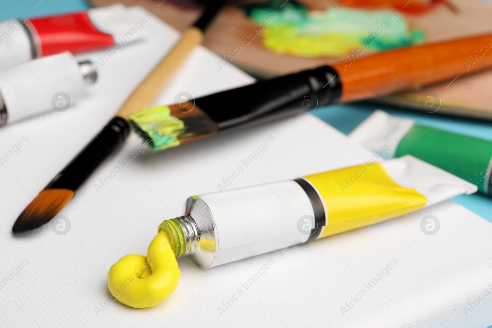 Photo of Tube with yellow oil paint and brushes on blank canvas, closeup