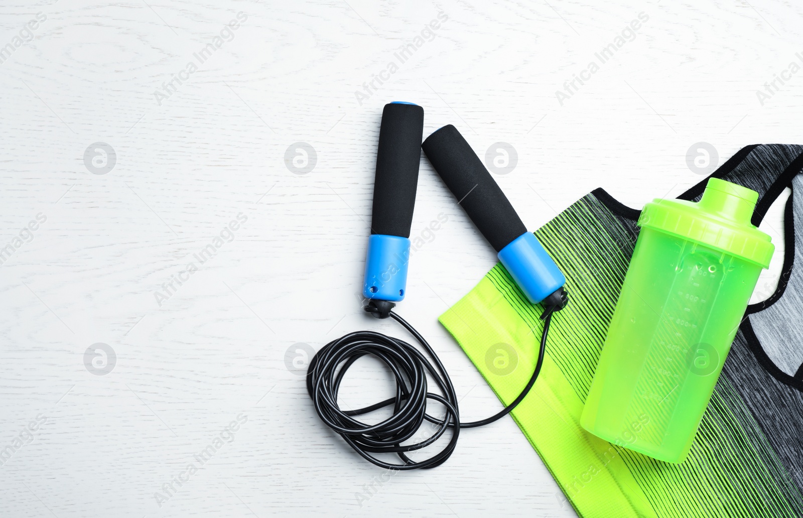 Photo of Flat lay composition with jump rope, gym equipment and space for text on white wooden background