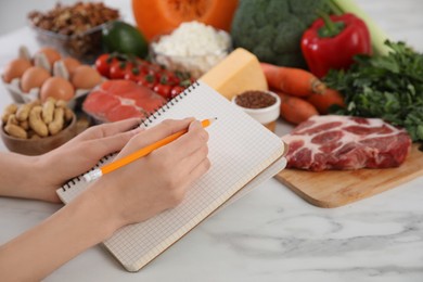Photo of Woman with notebook and healthy food at white table, closeup. Keto diet