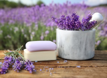 Fresh lavender flowers, soap bars and white marble mortar on wooden table outdoors, closeup