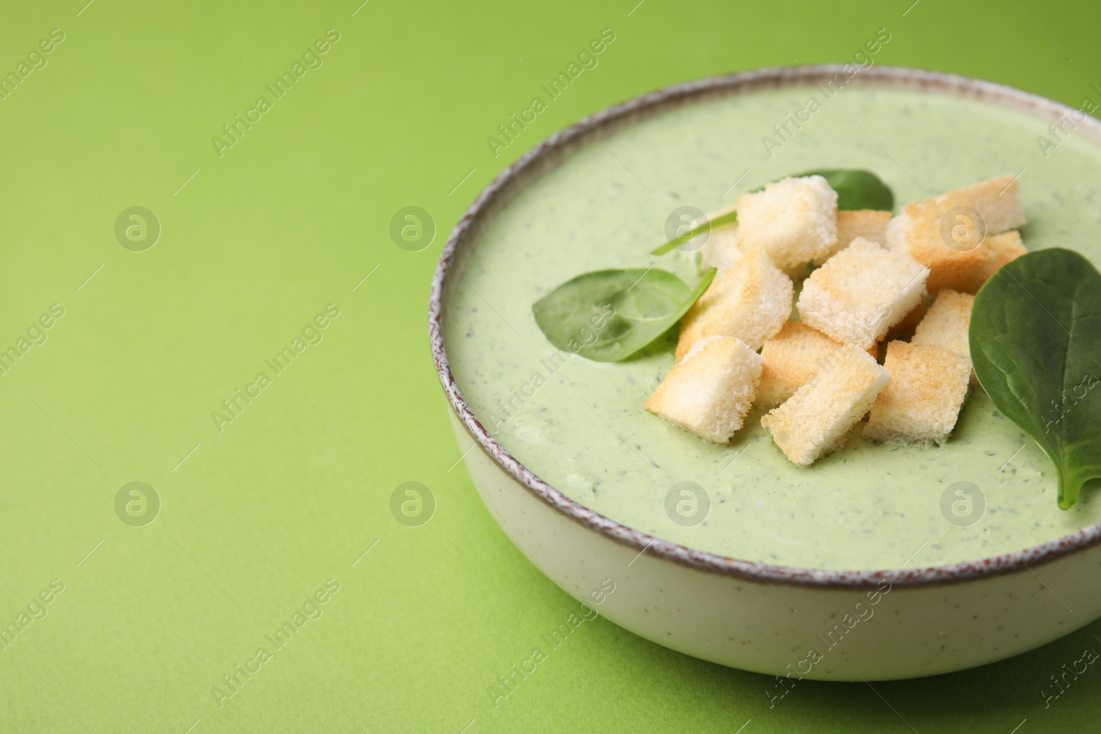 Photo of Delicious spinach cream soup with leaves and croutons in bowl on green background, space for text