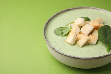 Delicious spinach cream soup with leaves and croutons in bowl on green background, space for text