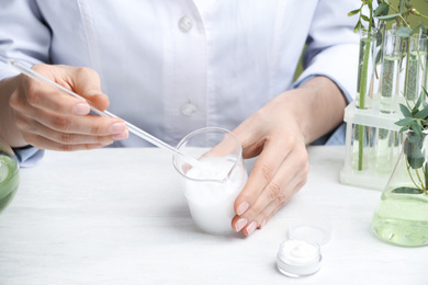 Photo of Woman working with cream at table in cosmetic laboratory, closeup