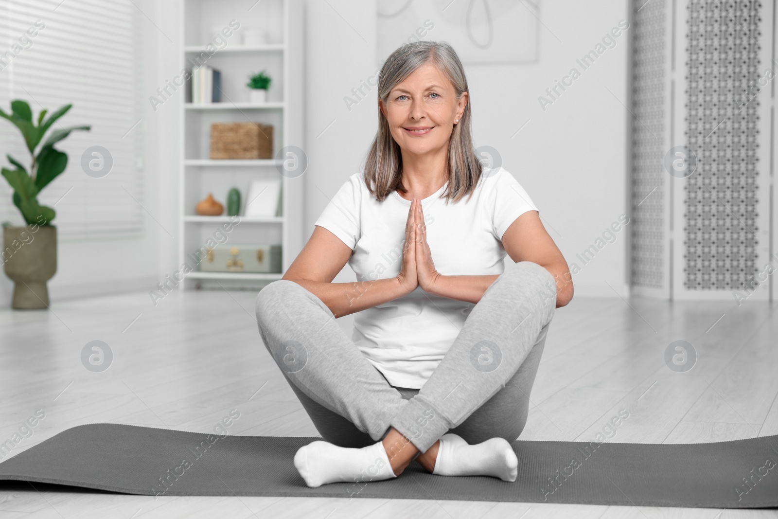 Photo of Happy senior woman practicing yoga on mat at home