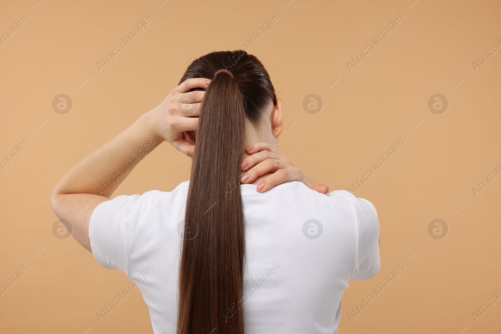 Photo of Woman touching her neck and head on beige background, back view