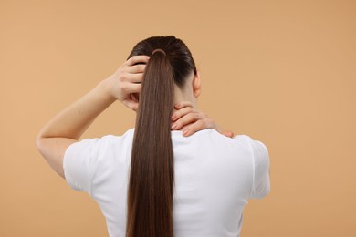 Woman touching her neck and head on beige background, back view