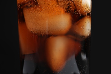 Photo of Glass of tasty refreshing cola with ice cubes on black background, closeup