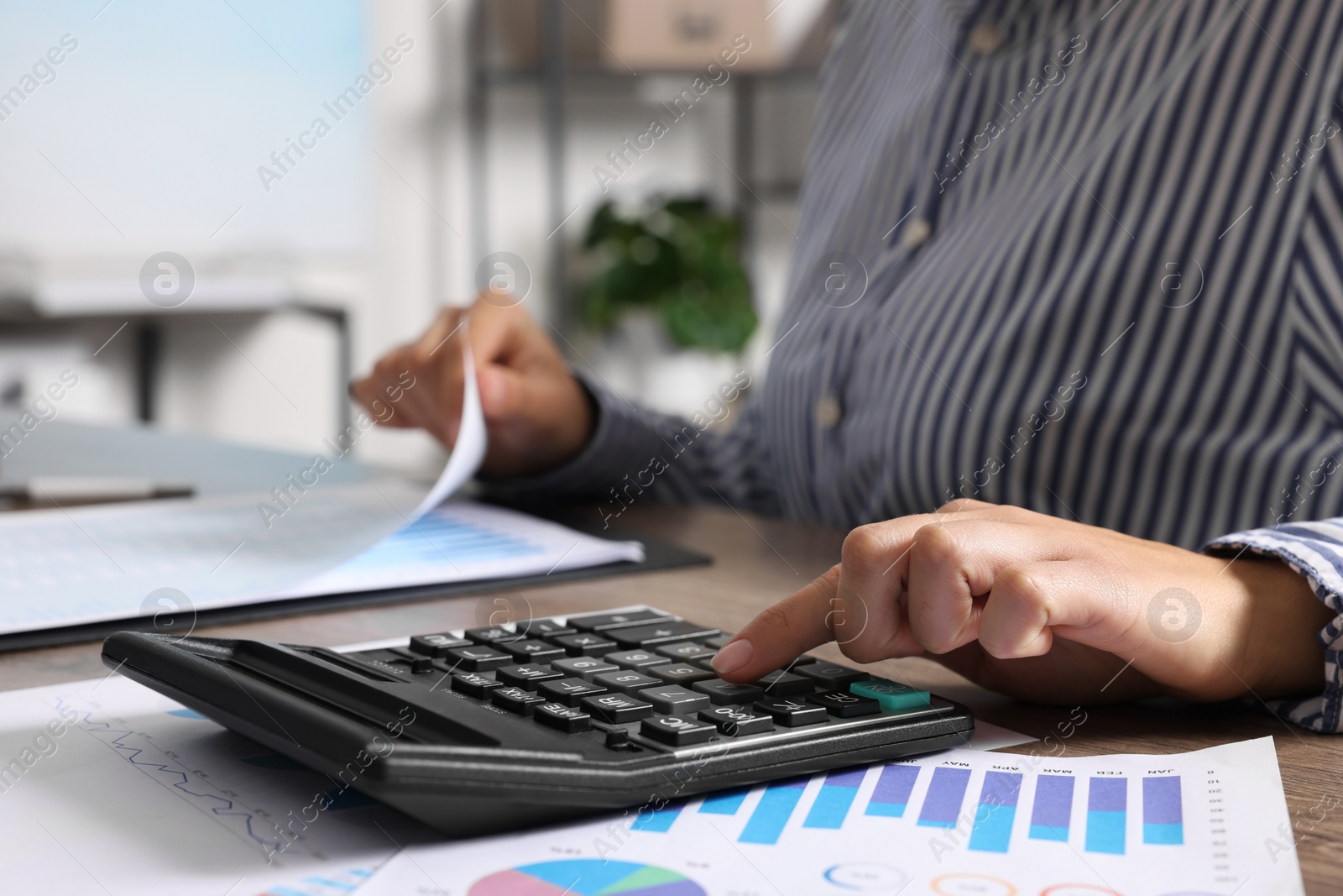 Photo of Woman using calculator at table indoors, closeup