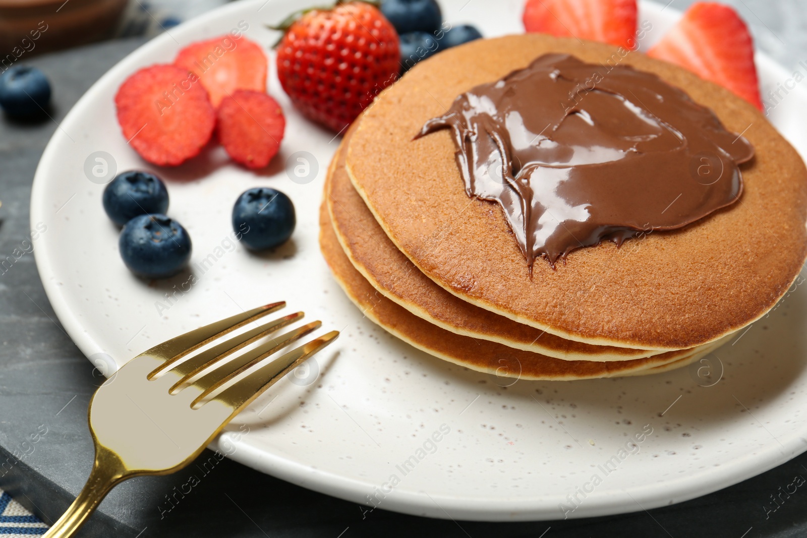 Photo of Tasty pancakes with chocolate paste, berries and fork on table, closeup