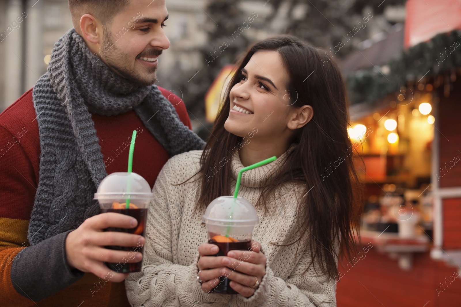 Photo of Young couple with cups of mulled wine at winter fair