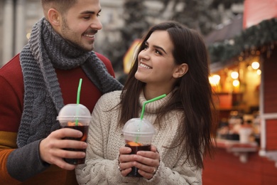 Young couple with cups of mulled wine at winter fair