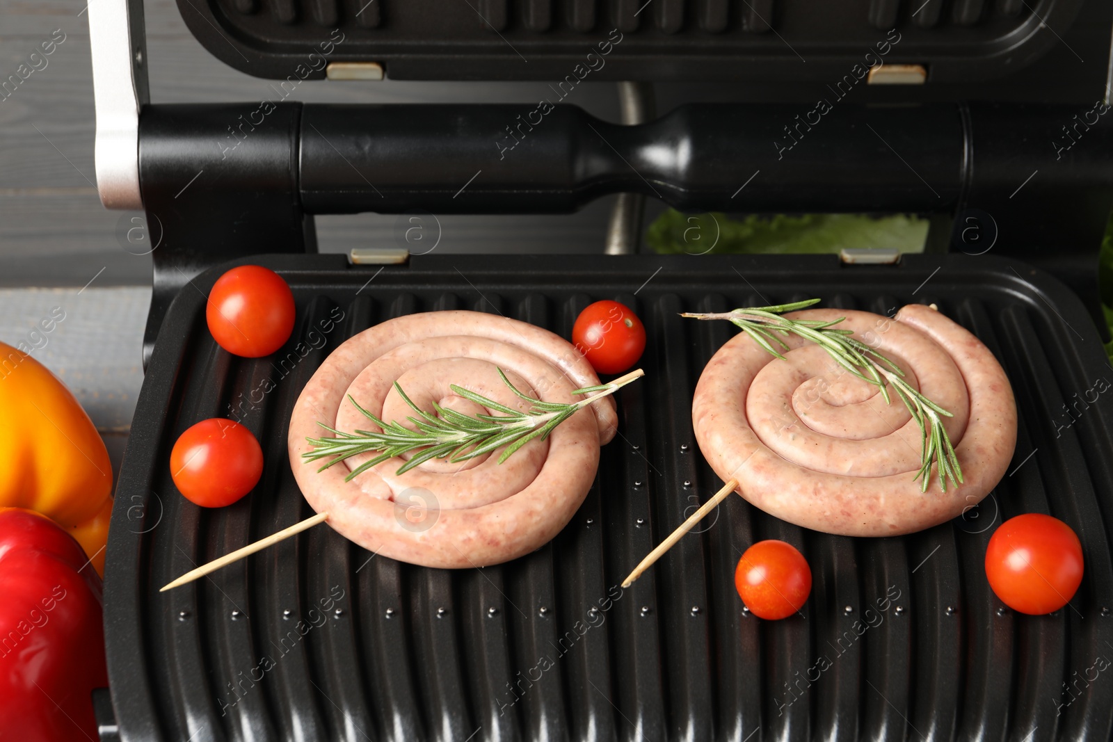 Photo of Electric grill with homemade sausages, rosemary and tomatoes on table, closeup