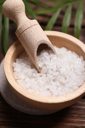 Photo of Sea salt in bowl and green leaves on wooden table, closeup. Spa product