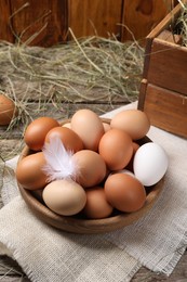 Fresh chicken eggs in bowl and dried hay on wooden table