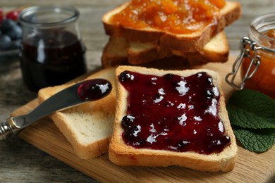 Photo of Delicious toasts with jams on wooden board, closeup