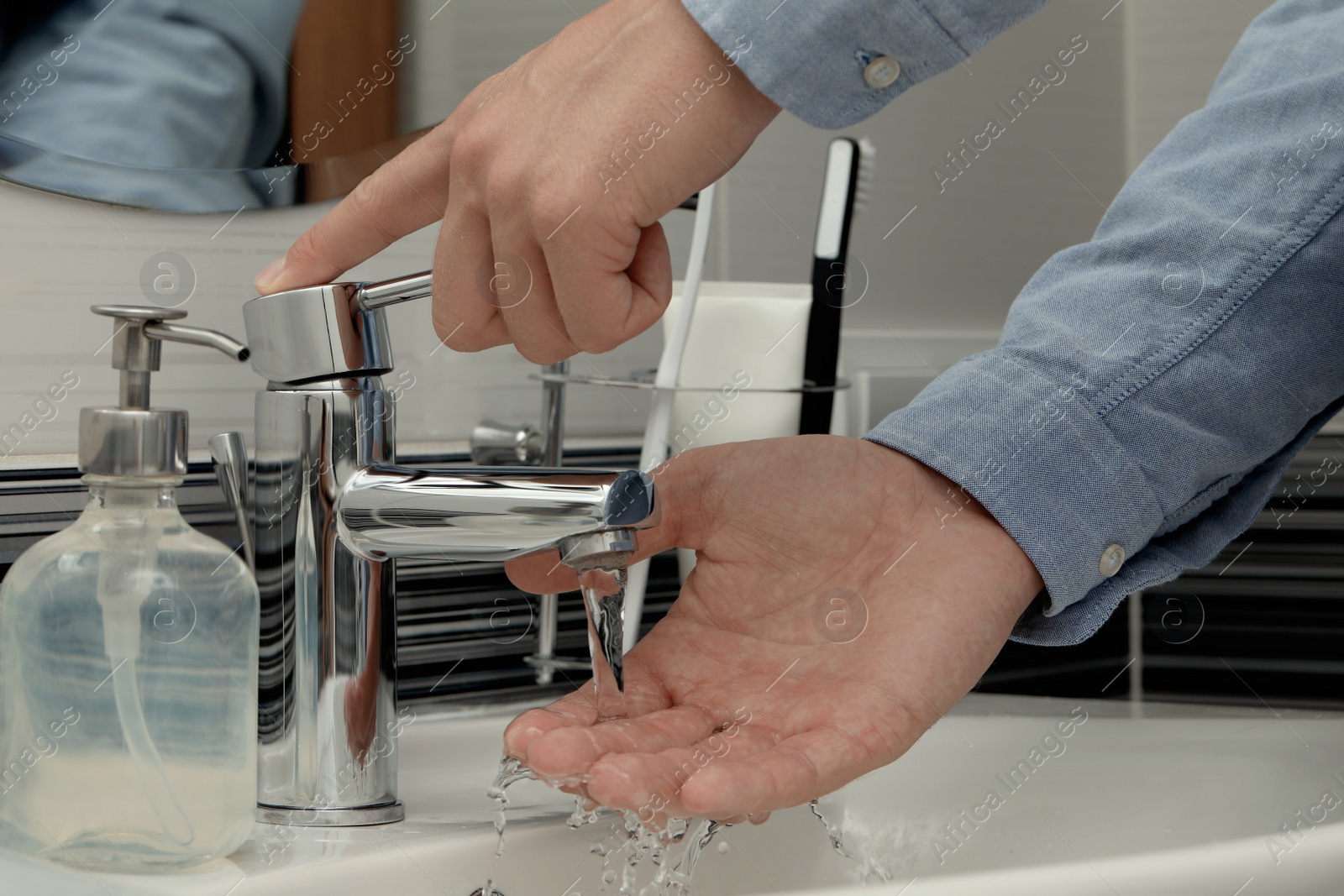 Photo of Man using water tap to wash hands in bathroom, closeup