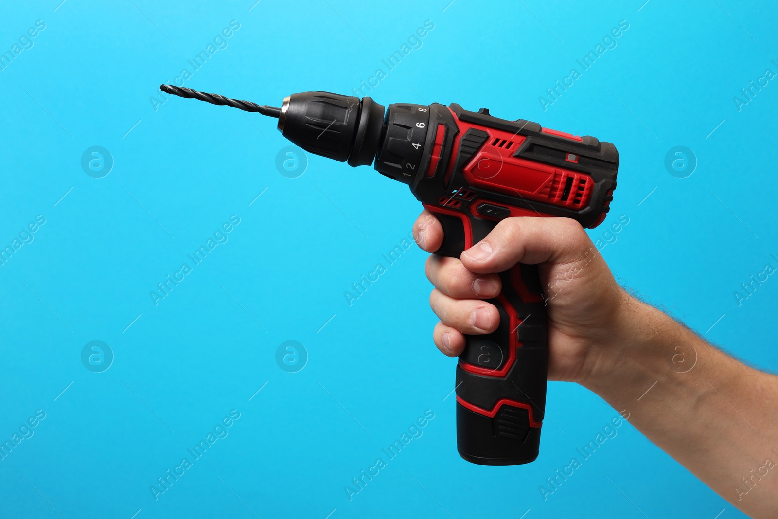 Photo of Handyman holding electric screwdriver on light blue background, closeup