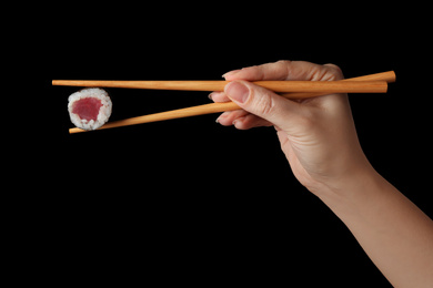 Photo of Woman holding sushi roll with chopsticks on black background, closeup