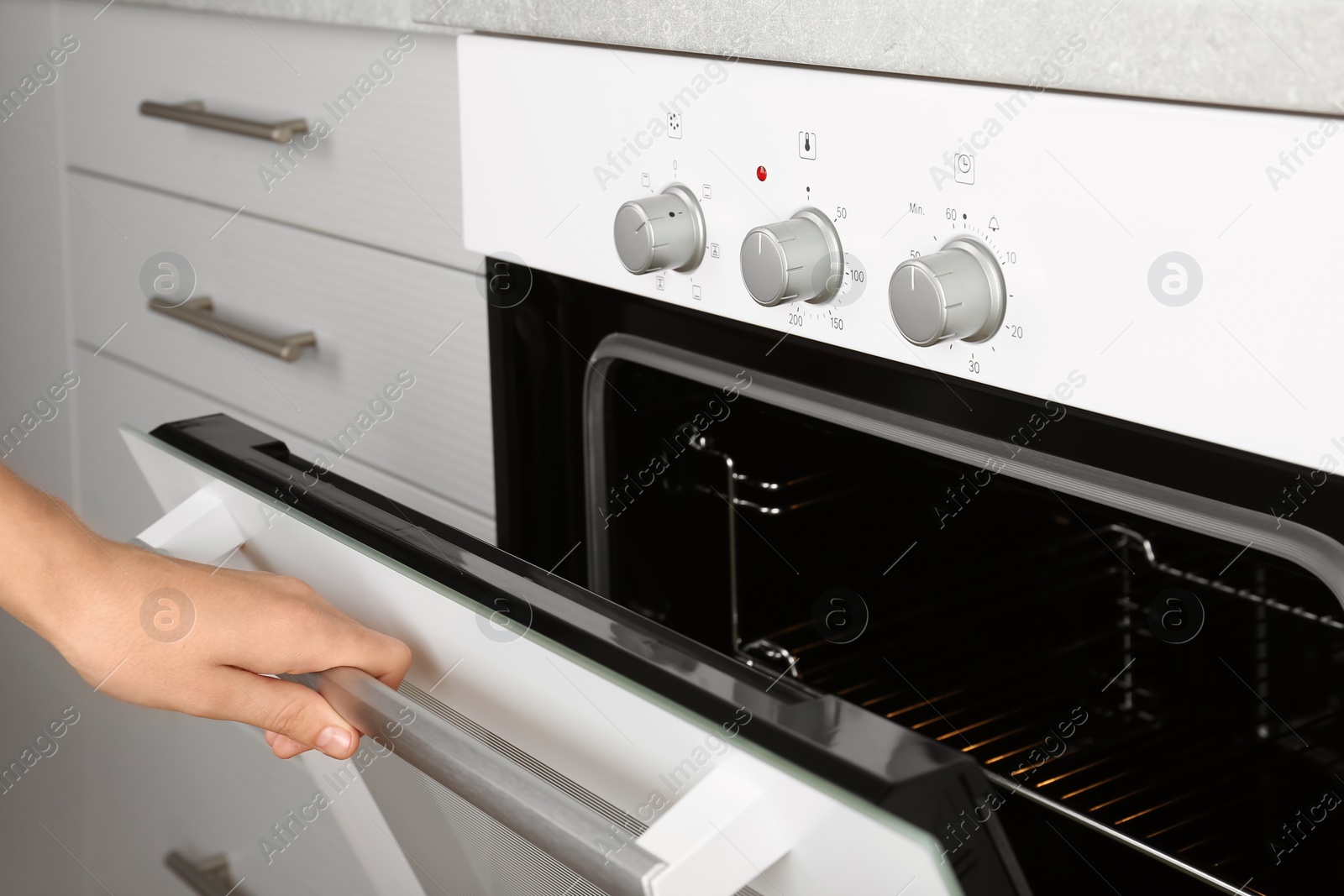 Photo of Woman opening empty electric oven in kitchen, closeup