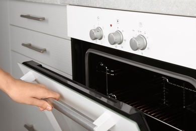 Photo of Woman opening empty electric oven in kitchen, closeup