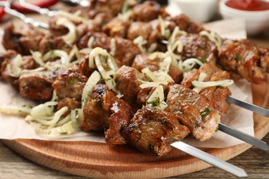 Metal skewers with delicious meat and onion served on wooden table, closeup