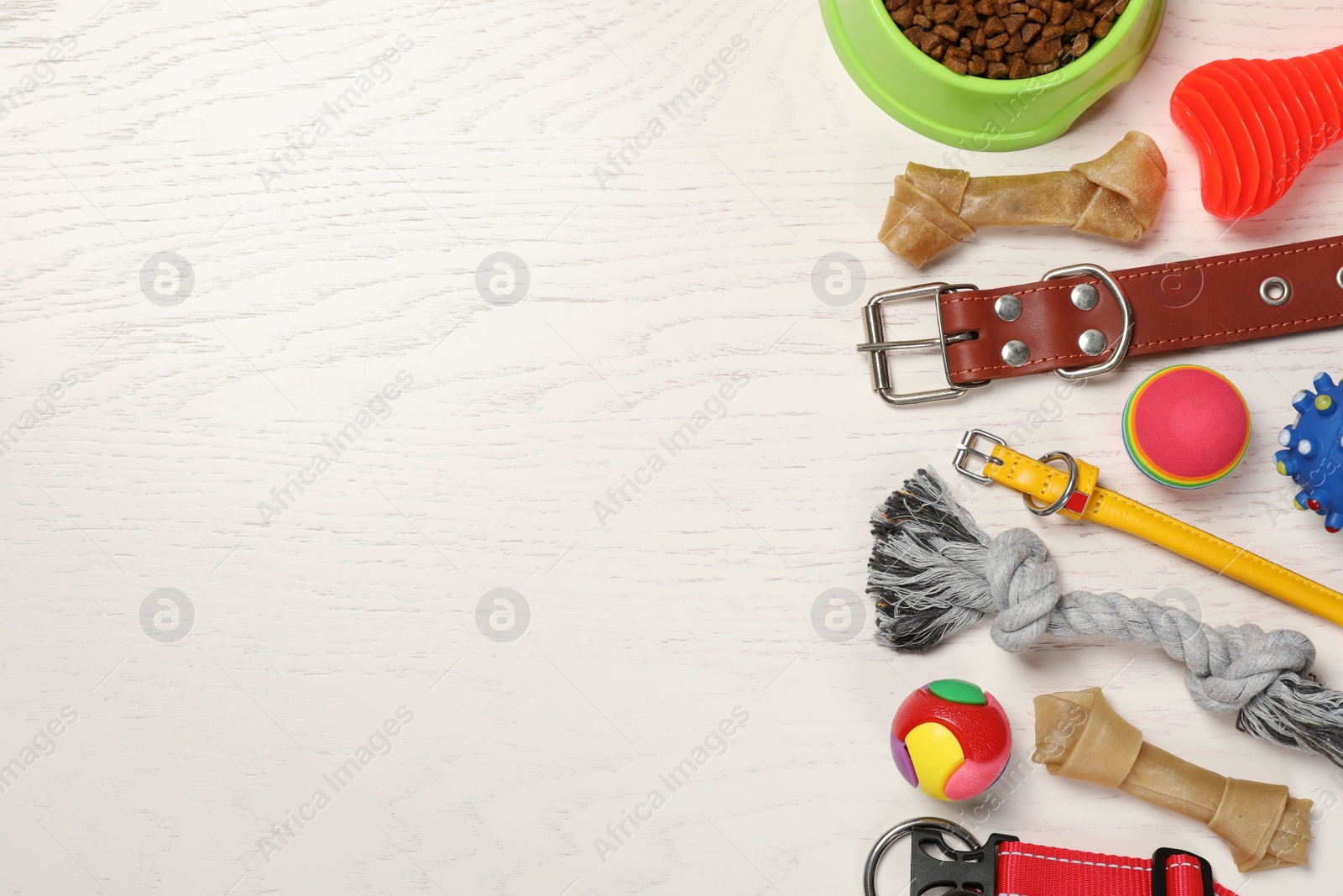 Photo of Flat lay composition with dog collars, toys and food on white wooden table. Space for text