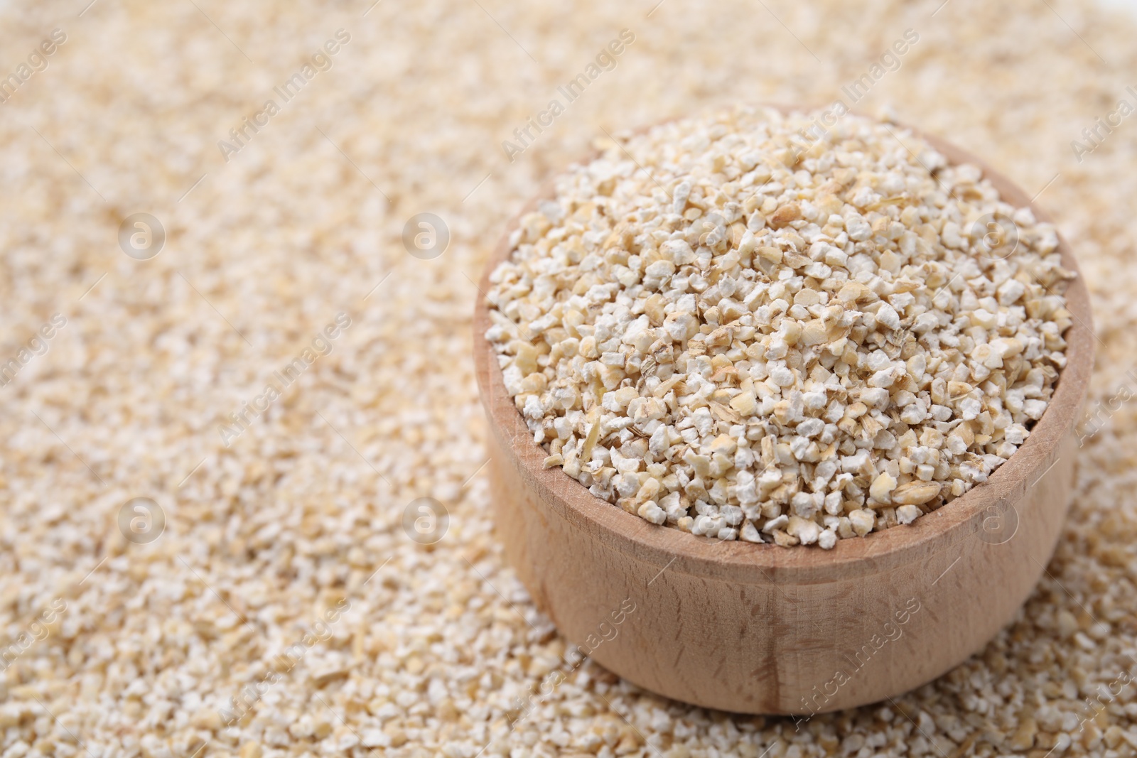 Photo of Wooden bowl on raw barley groats, closeup. Space for text