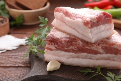 Photo of Pieces of tasty pork fatback with garlic and parsley on wooden table, closeup