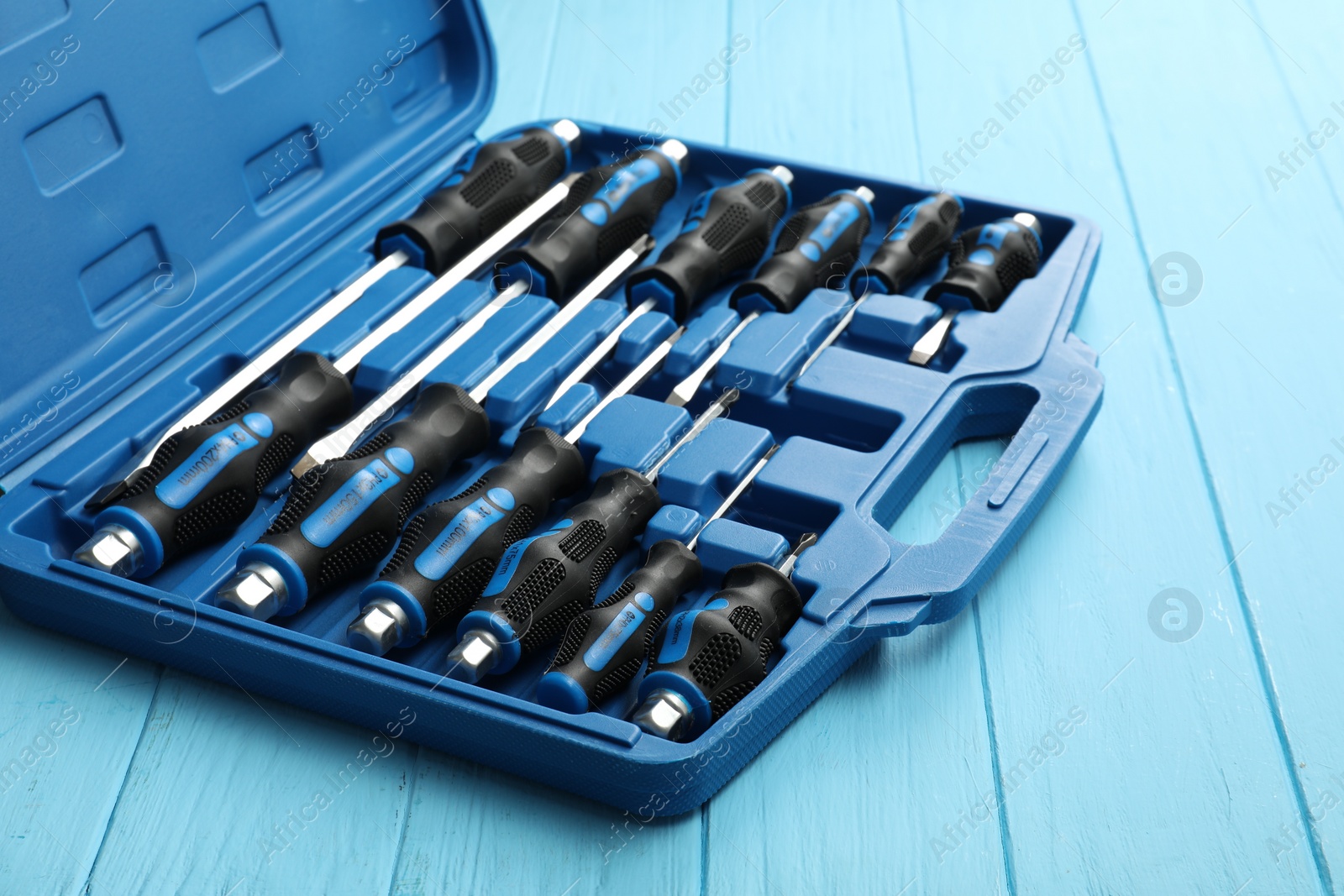 Photo of Set of screwdrivers in open toolbox on light blue wooden table, closeup