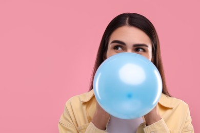 Photo of Woman inflating light blue balloon on pink background, space for text