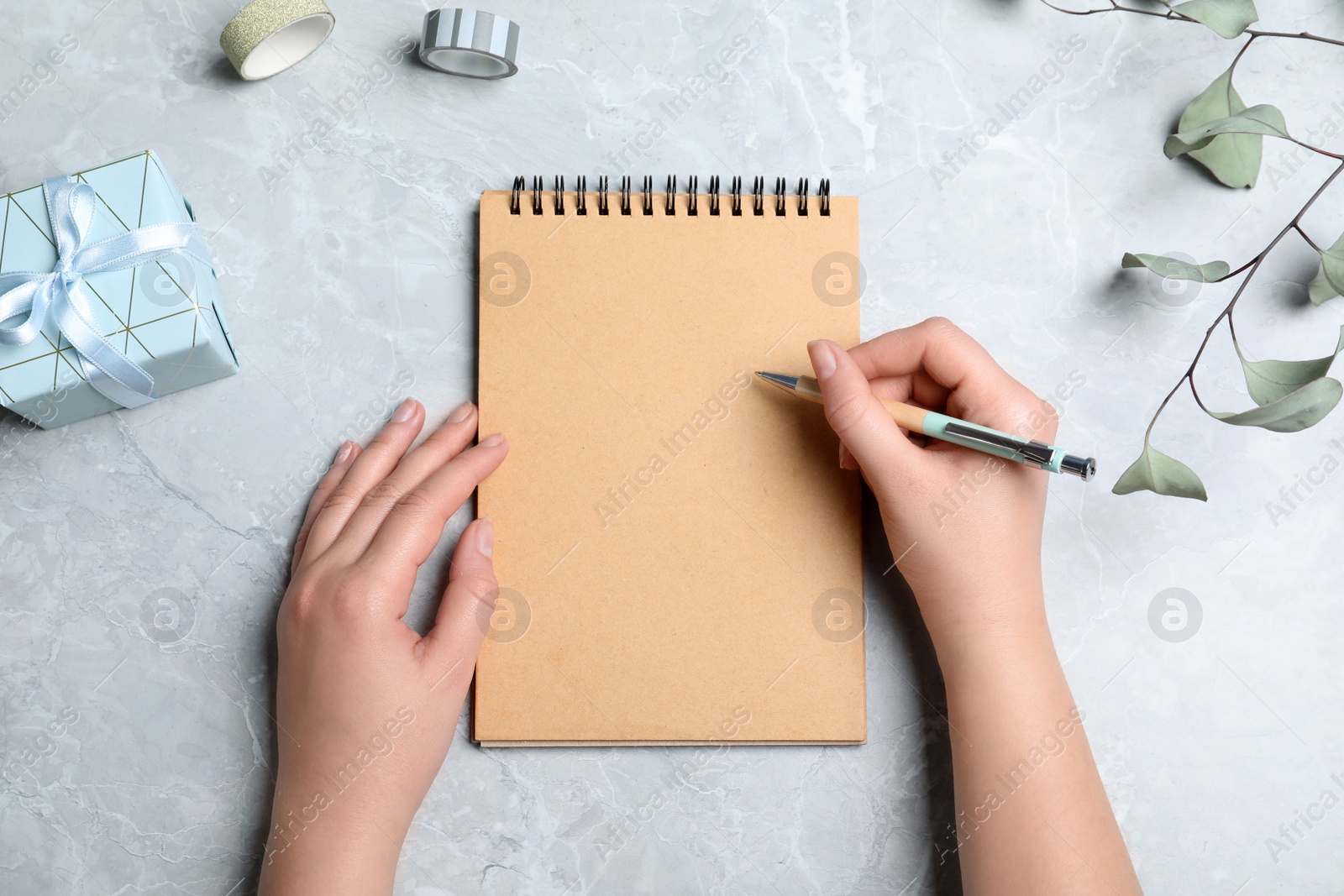 Photo of Woman with pen and blank notebook at grey table, top view