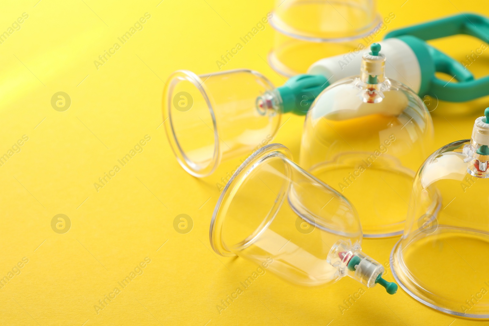 Photo of Plastic cups and hand pump on yellow background, closeup with space for text. Cupping therapy