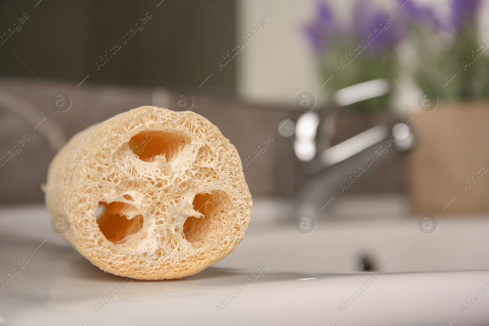 Photo of Natural loofah sponge on washbasin in bathroom, closeup. Space for text