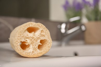 Photo of Natural loofah sponge on washbasin in bathroom, closeup. Space for text