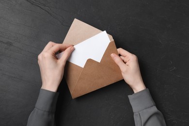 Photo of Woman taking card out of letter envelope at black textured table, top view