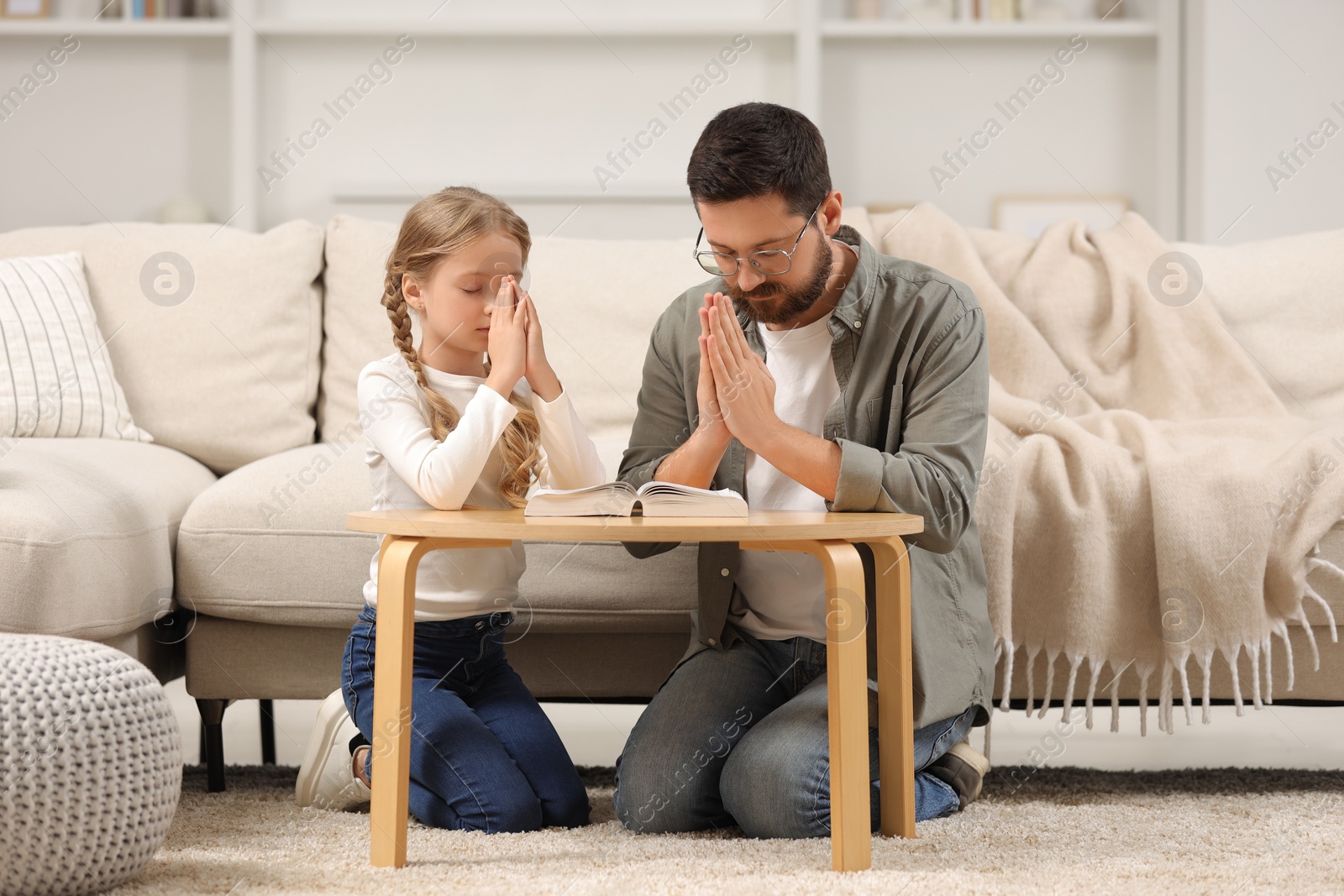 Photo of Girl and her godparent praying over Bible together at table indoors