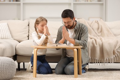 Girl and her godparent praying over Bible together at table indoors