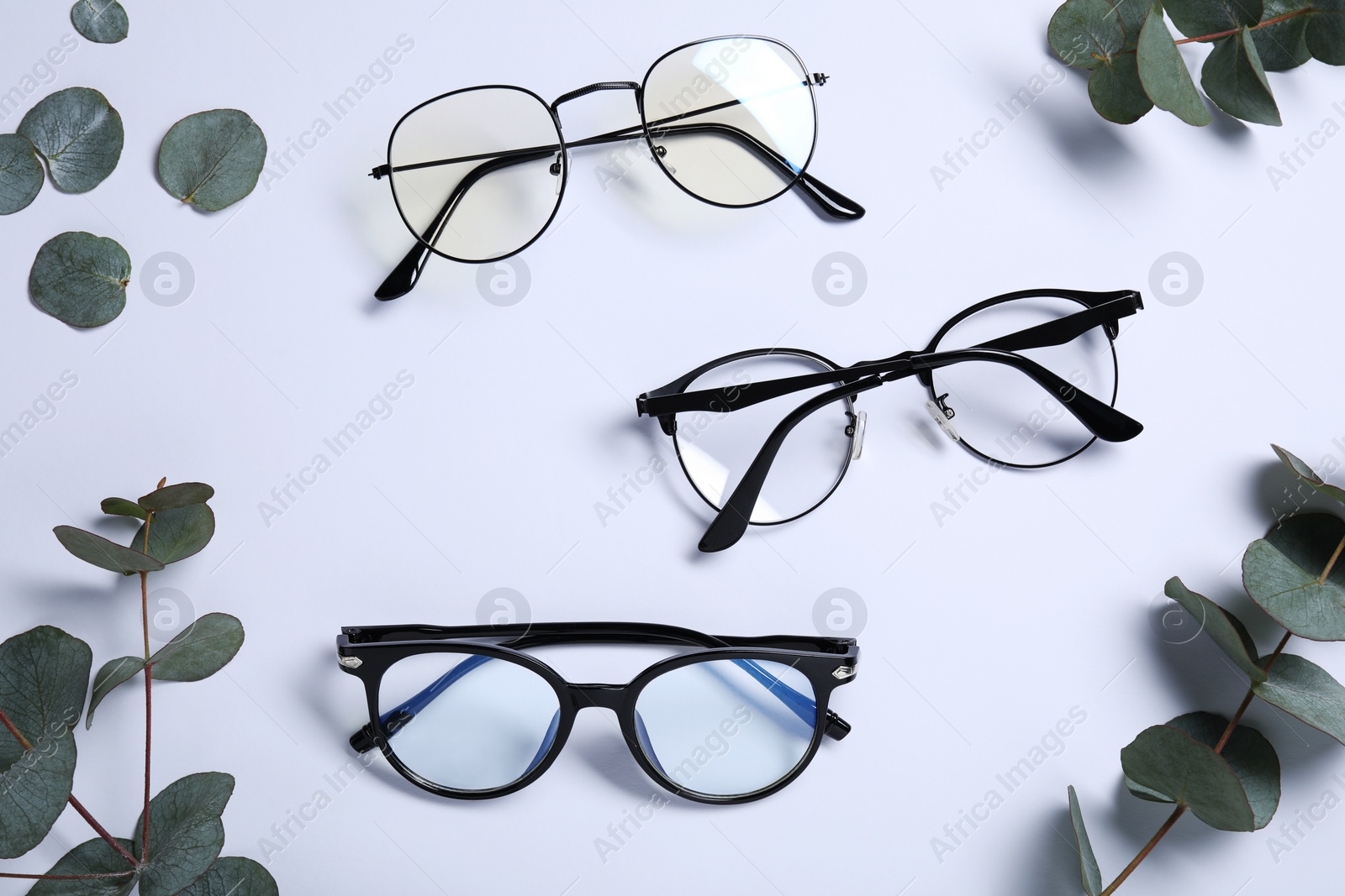 Photo of Different stylish glasses and eucalyptus leaves on white background, flat lay