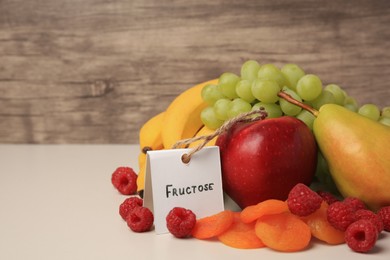 Photo of Card with word Fructose, delicious ripe fruits, raspberries and dried apricots on beige table, space for text