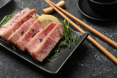 Photo of Pieces of delicious tuna steak served on black table, closeup