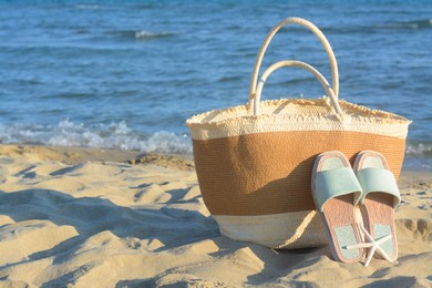 Photo of Straw bag, slippers and dry starfish on sandy beach near sea, space for text