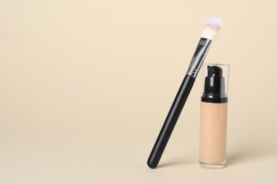 Photo of Bottle of skin foundation and brush on beige background, space for text. Makeup product