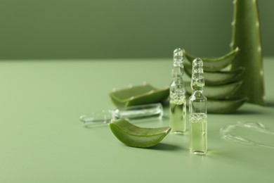 Photo of Skincare ampoules with extract of aloe vera and cut green leaves on color background. Space for text