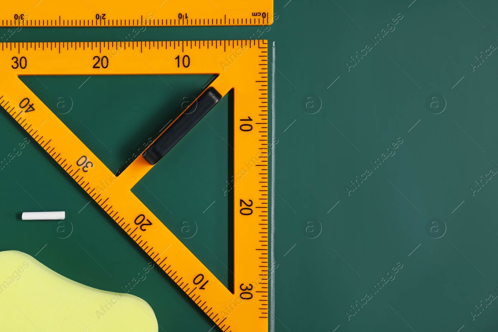 Photo of Protractor, sponge, chalk and ruler on green chalkboard, flat lay. Space for text