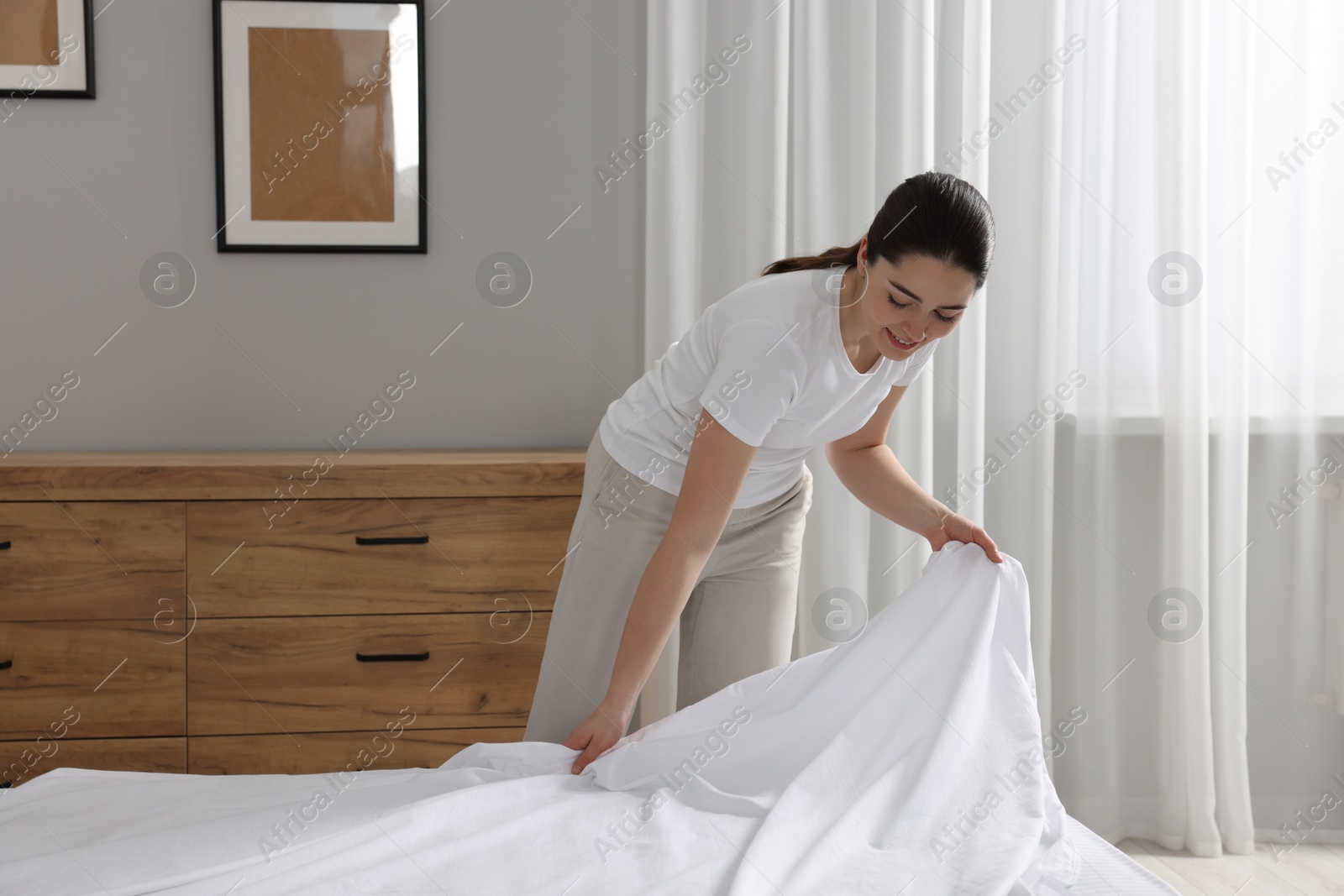 Photo of Young woman changing bed linens at home