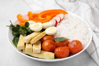 Delicious poke bowl with basil, vegetables, eggs and tofu on light grey table, closeup
