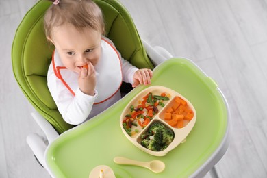 Photo of Cute little baby eating food in high chair indoors, above view